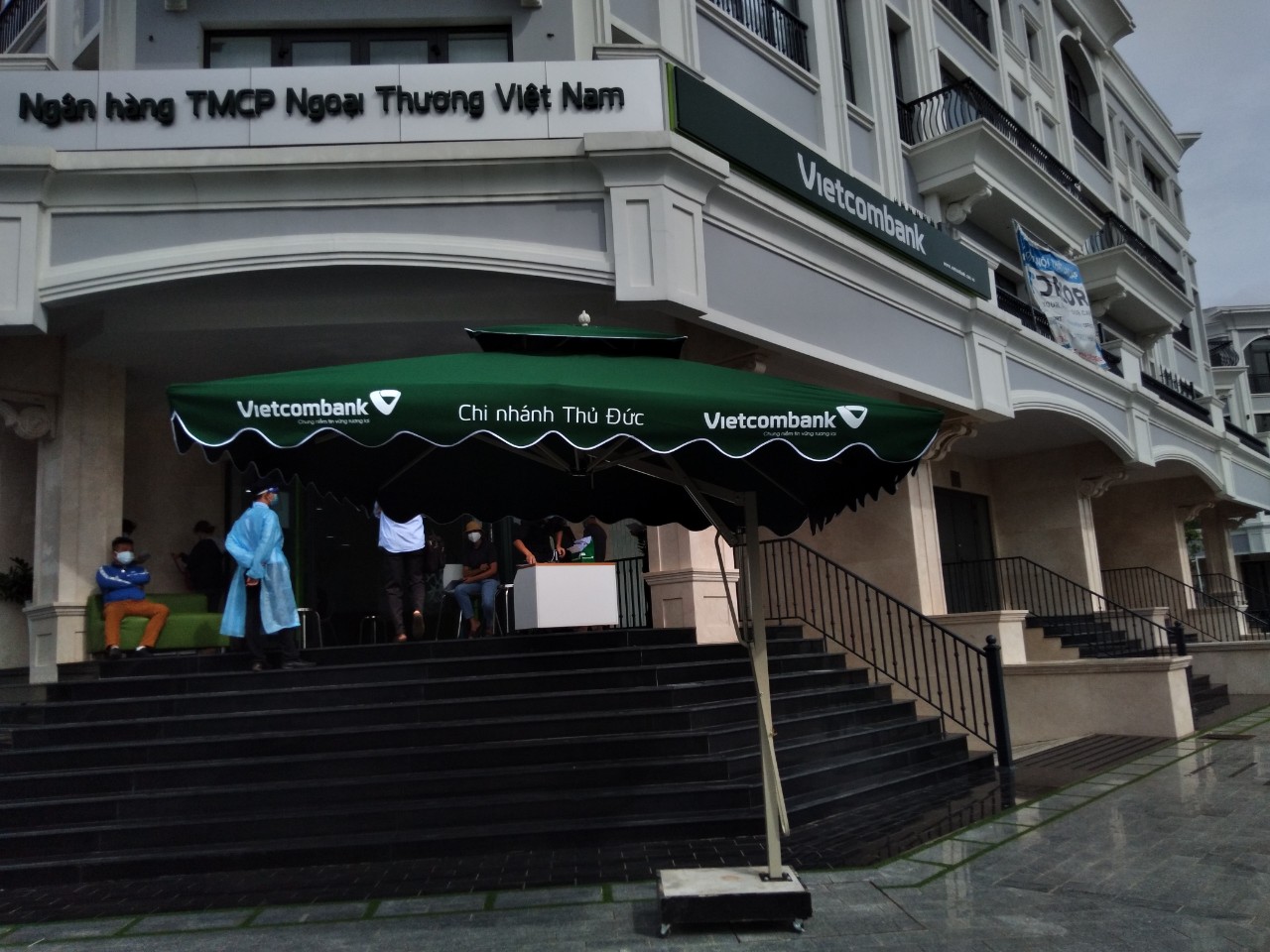 Dù lệch tâm vuông in tên Vietcombank Chi nhánh Thủ Đức trước bậc thềm lên sảnh.