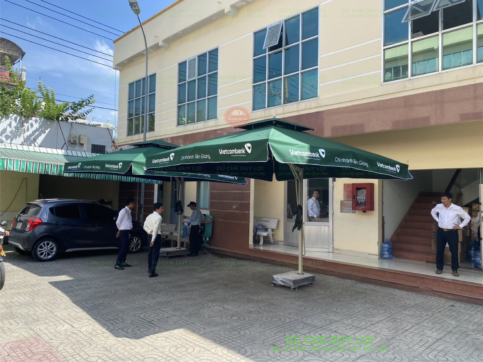 Dù Vietcombank màu xanh rêu trước công trình có bậc thềm và khoảng sân.