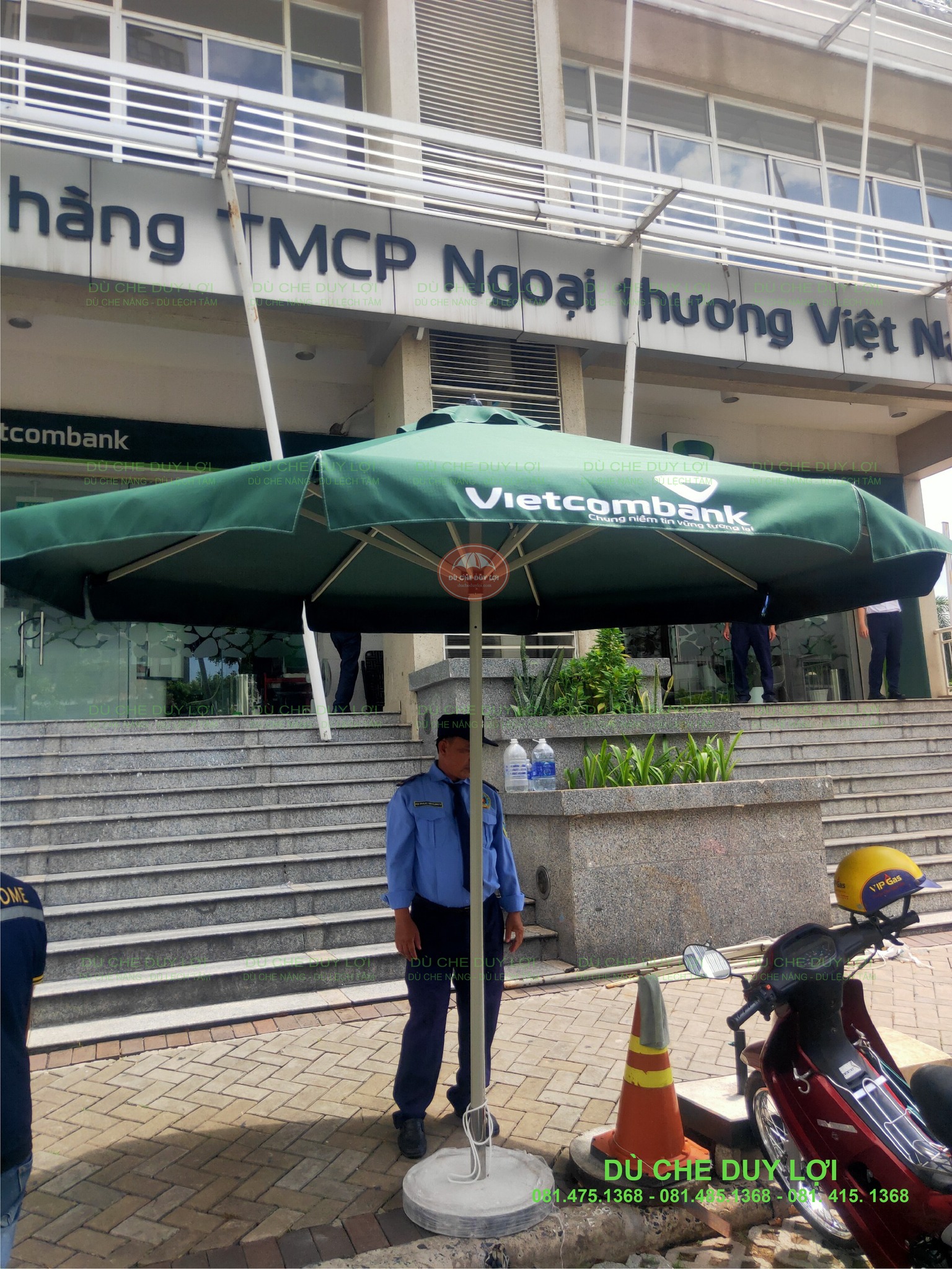 Dù tròn đúng tâm Vietcombank với trụ giữa tán và đế tròn gần bậc thềm.