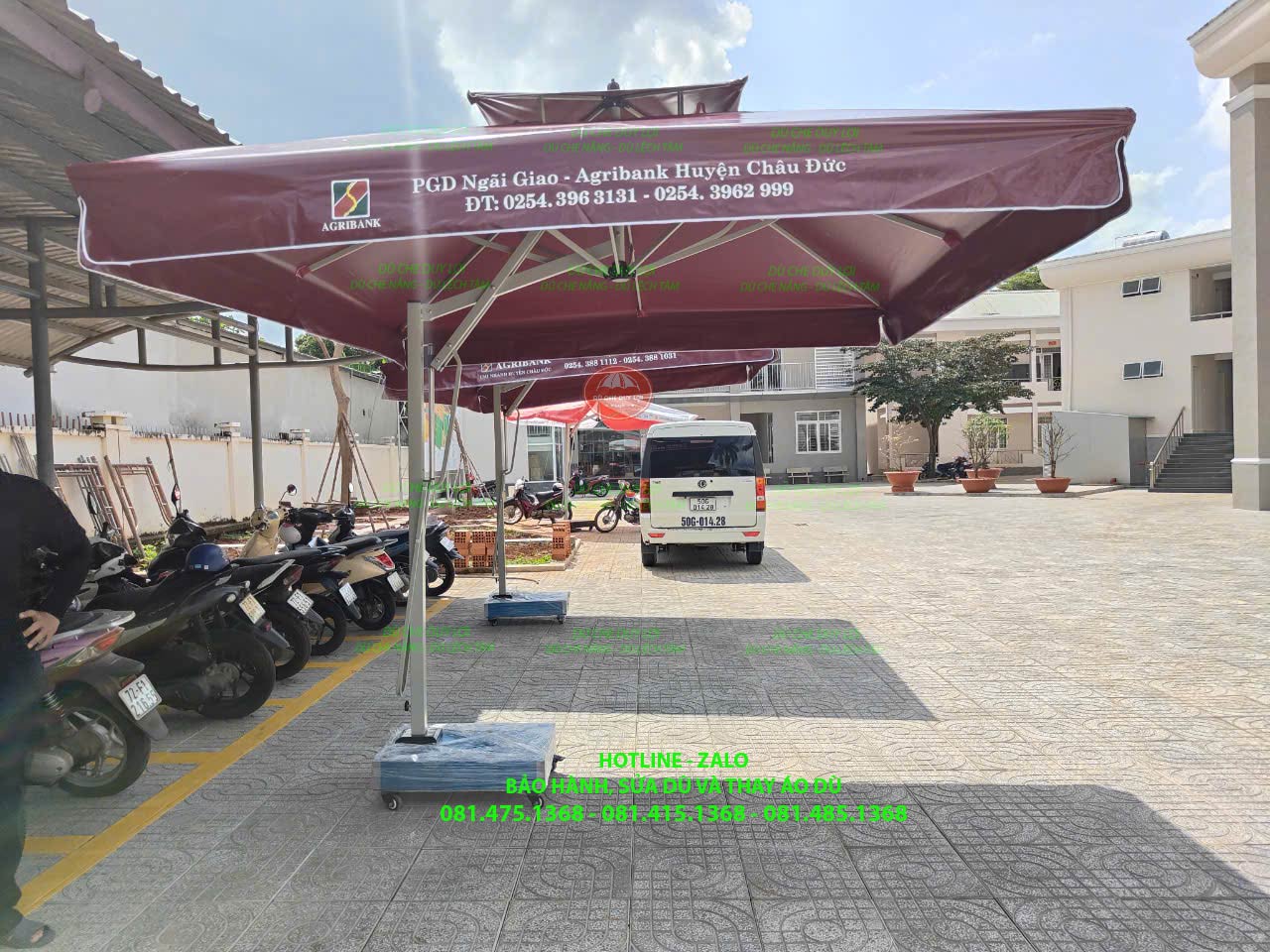 Dù lệch tâm vuông hai tầng màu đỏ sẫm in thông tin phòng giao dịch Agribank tại sân để xe.