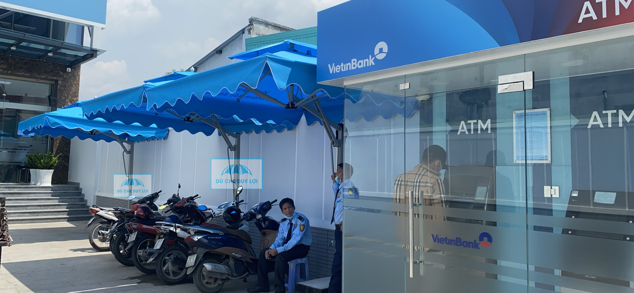 Các tán dù xanh cạnh khu vực ATM VietinBank và nơi nhân viên hướng dẫn khách.